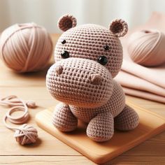 a crocheted hippo sits on a cutting board next to balls of yarn