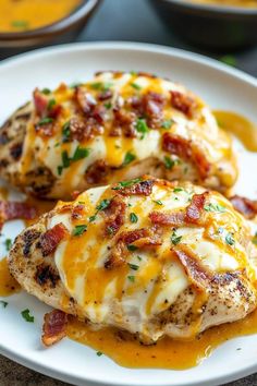 two pieces of chicken covered in cheese and bacon on a white plate with orange sauce