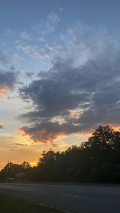 the sun is setting behind some clouds in the sky over a road and street sign