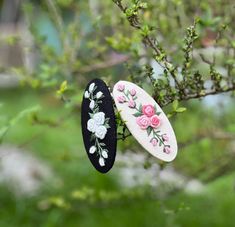 two black and white hair clips with pink roses on them hanging from a tree branch