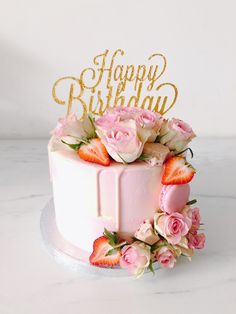 a white cake with pink flowers and gold happy birthday topper