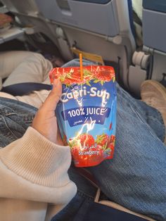 someone is holding up a carton of juice in their hand while sitting on an airplane