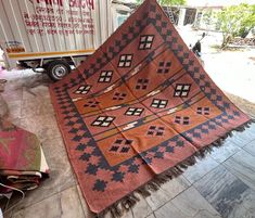 an orange and black blanket on the ground next to a truck