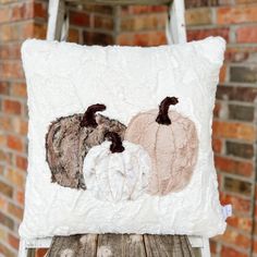 a white pillow with three pumpkins on it sitting on top of a wooden table