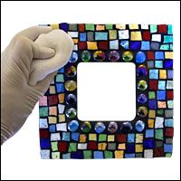 a gloved hand is holding up a multicolored glass tile photo frame with white background