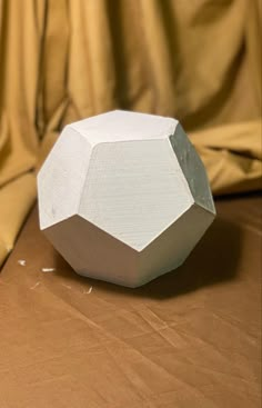 a white object sitting on top of a brown tablecloth covered floor next to a curtain