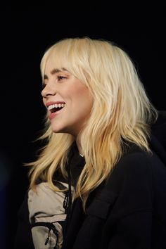 a woman with blonde hair smiling and looking to the side while wearing a black jacket