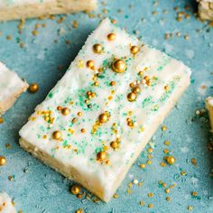 white frosted cake with gold sprinkles on blue surface next to other cakes