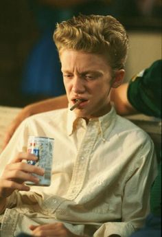 a young man sitting on a couch drinking from a can