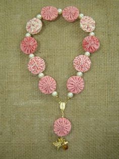 a pink and white beaded necklace with flowers on it's end, surrounded by pearls