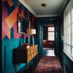 A hallway with teal wainscoting and multicolored geometric wallpaper. There is a wooden sideboard with a lamp, two blue vases, and a red bowl on top. A rectangular mirror hangs above the sideboard. A red patterned runner rug leads to a room with a window and a red sofa. Bold Foyer, Jewel Tones Interior Design, Entrance Inspiration, Art Deco Hallway, Modern Entryway Decor, Traditional Entryway, Hallway Inspiration