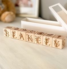 a wooden block with the word lake spelled in gold ink on it sitting on a table next to a teddy bear