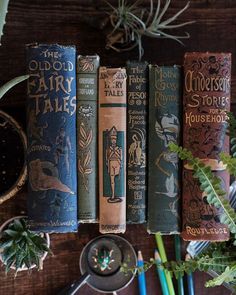 an assortment of books sitting on top of a wooden table next to plants and scissors