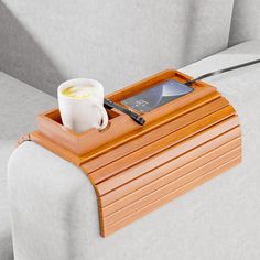 a wooden tray with a cell phone on it sitting on a couch next to a cup of coffee