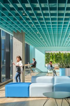 people sitting at tables in an office with blue couches and green plants on the walls