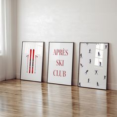 three framed ski posters sitting on top of a hard wood floor next to a window