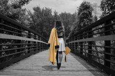 a woman walking across a bridge with a yellow jacket over her shoulders and an orange umbrella