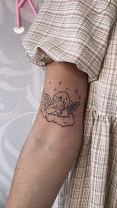 a woman's arm with a tattoo on it that has an angel sitting on top of a cloud