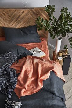 a bed with an orange blanket and some books on top of it next to a potted plant