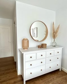 a white dresser topped with a mirror and a vase filled with dried pamodia