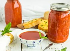 a bowl of tomato sauce next to some bread and butter on a white wooden table