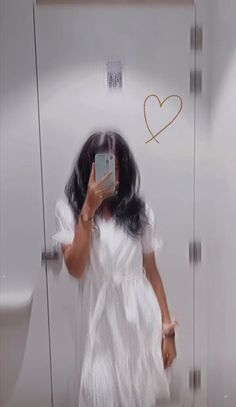 a woman taking a selfie in front of a urinal with a heart drawn on it