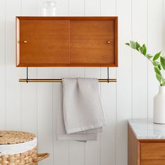 a wooden cabinet hanging on a wall next to a basket with towels and a potted plant