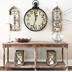 a large clock mounted to the wall above a table with vases and candles on it