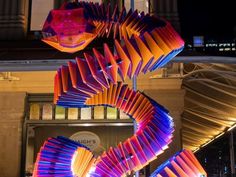 an artistic sculpture is displayed in front of a building with lights on the outside and inside