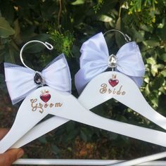 two bride and groom hangers with matching bows on them, one has a crystal heart in the middle