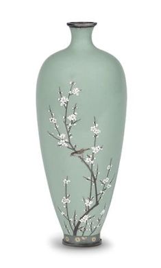 a green vase with white flowers painted on the front and side, sitting against a white background