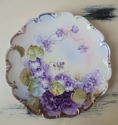 a white plate with purple flowers and leaves painted on the side, sitting on a table