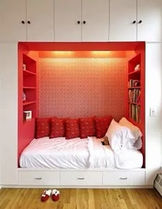 a bedroom with red and white walls, built in bookshelves and lots of pillows