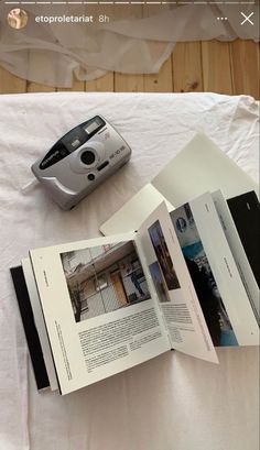 an open book and camera sitting on top of a white table cloth covered bed spread