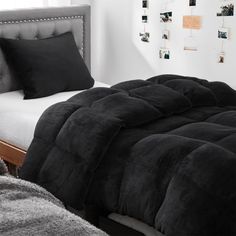 a bed with black comforter and pillows in a bedroom next to a white wall