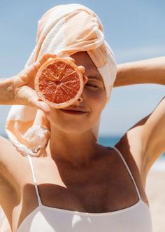 a woman with a towel on her head holding up an orange slice to her face