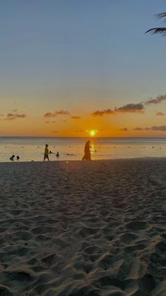 the sun is setting at the beach with people walking on the sand and in the water