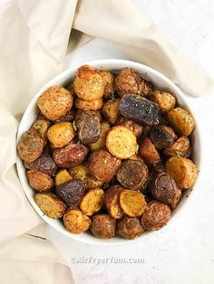 a white bowl filled with roasted potatoes on top of a table next to a napkin