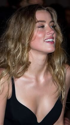 a close up of a person wearing a black dress and smiling at someone behind her