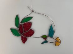 a glass ornament with two colorful birds hanging from it's side on a white wall