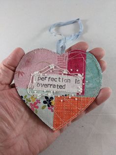 a hand holding a patchwork heart ornament that says imperfect affection is overrated