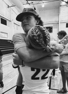 two girls hugging each other in a gym with one girl wearing a baseball cap and the other holding her