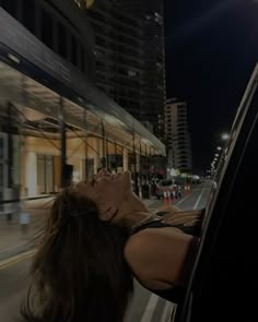 a woman laying down on the side of a bus at night with her eyes closed