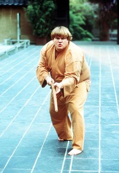 a man dressed in an orange outfit is holding a wooden stick while standing on the ground