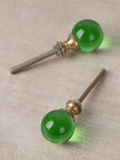 two green glass door knobs are on a white surface with a screw in the middle