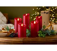 three red candles sitting on top of a wooden table next to presents and a christmas tree