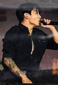 a male in a black shirt is holding a microphone and looking at the side of his face