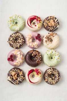 twelve donuts with different toppings are arranged in a circle on a white surface