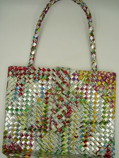 a multicolored woven bag hanging on a wall next to a white wall with a red, yellow, green, and blue striped handle