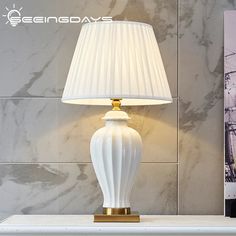 a white lamp sitting on top of a table next to a wall with a ship in the background